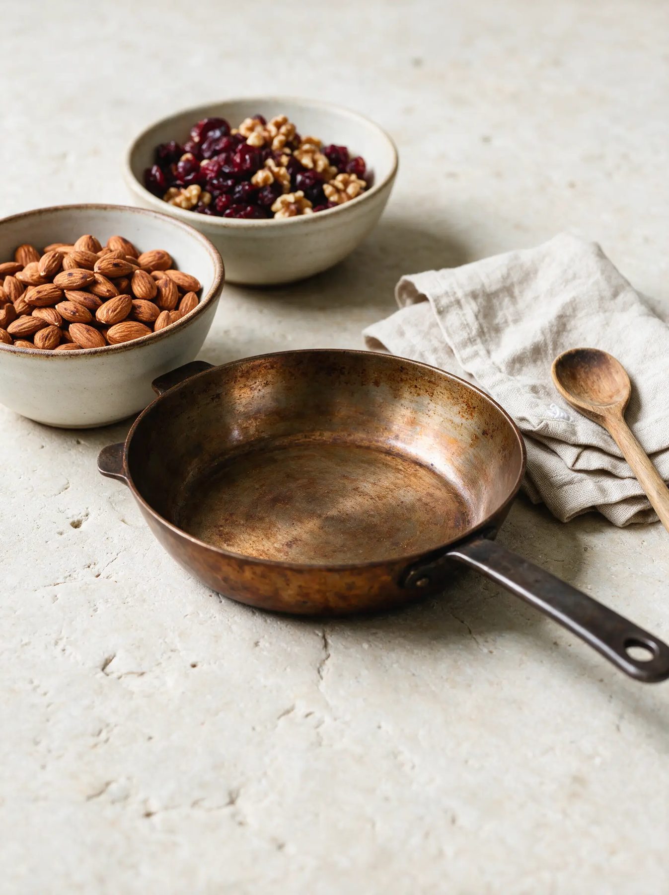 Carbon steel skillet, stoneware bowls and linen on pale stone
